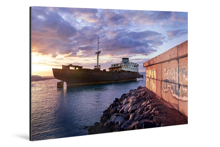 Rusting ghost ship floating near rocky shore under dramatic blue and purple sunset clouds. - 45 x 30cm / Photo hinter Acrylglas / Unframed