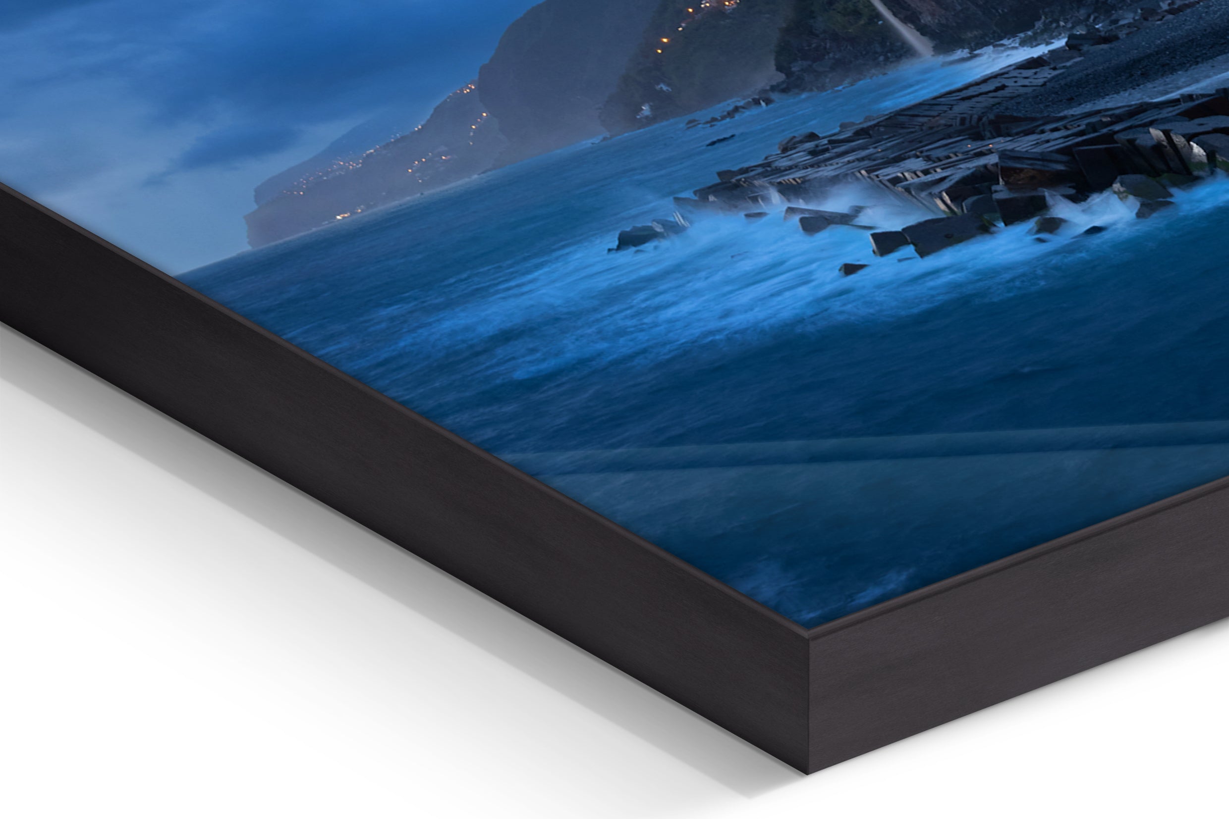 Close-up of black-framed panel print showing ocean waves and mountainous coastline under cloudy blue sky at dusk. - 90 x 38 cm / Photo hinter Acrylglas / Unframed